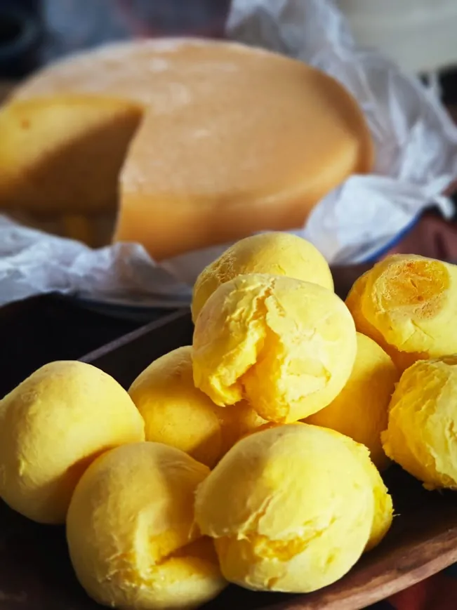 Pães de queijo ao lado de uma peça de queijo curado