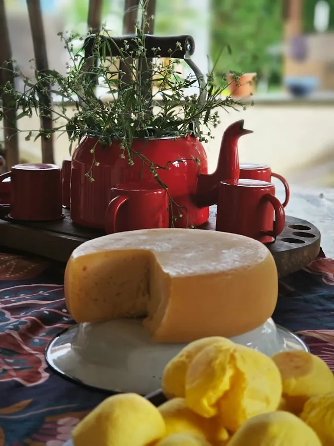Queijo na mesa de café com bule vermelho e pães de queijo