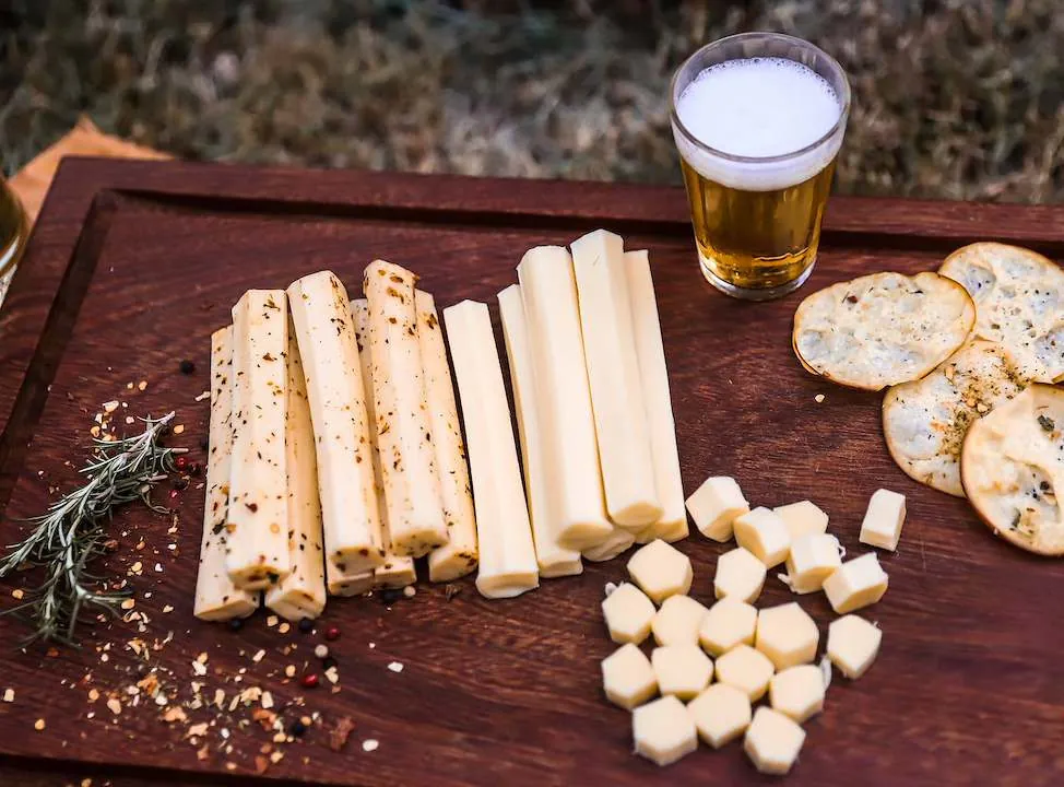Tábua de palitos temperados e puros, cubos de queijo e um copo de cerveja